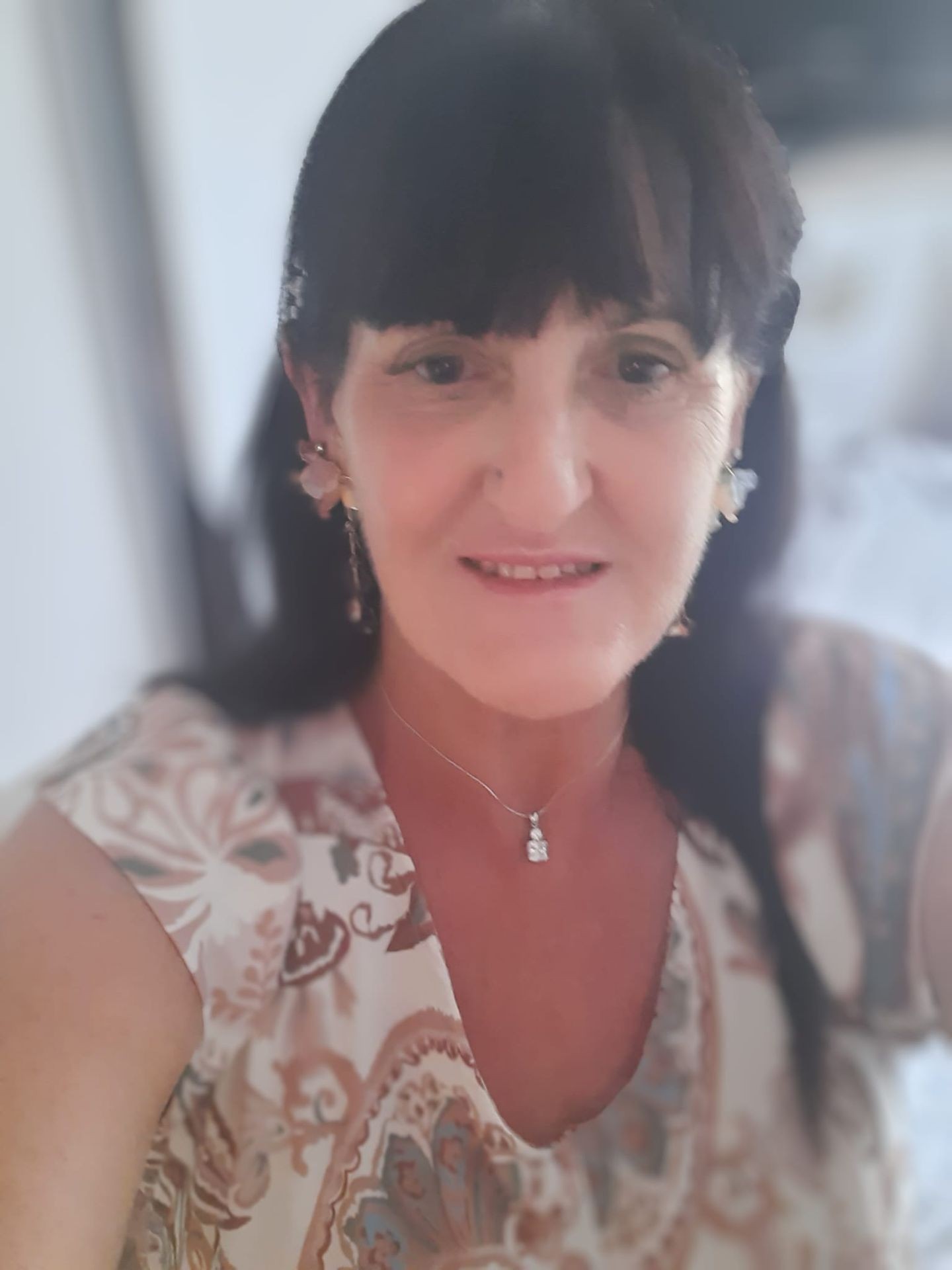 Woman with dark hair wearing patterned blouse and necklace, smiling at the camera.