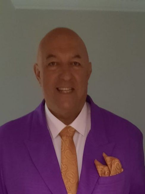 Man in purple suit with orange tie and pocket square smiling at the camera.